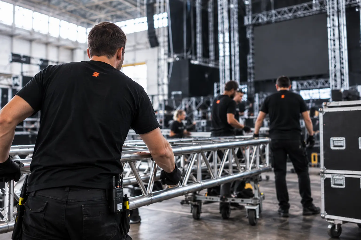Kleine crew in een geconcentreerde briefing tussen flightcases in een AV-magazijn.